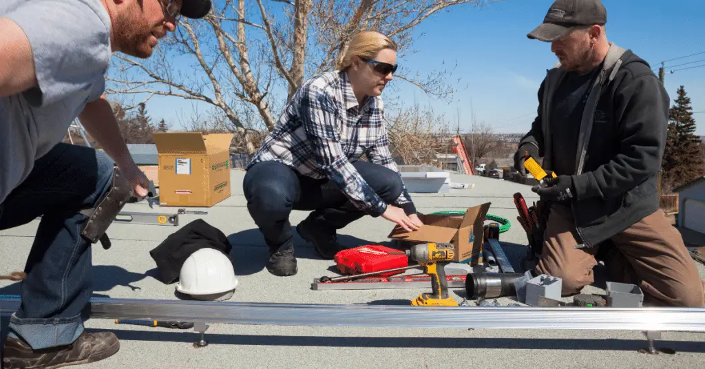 Two men and a woman on a roof during a solar installation process